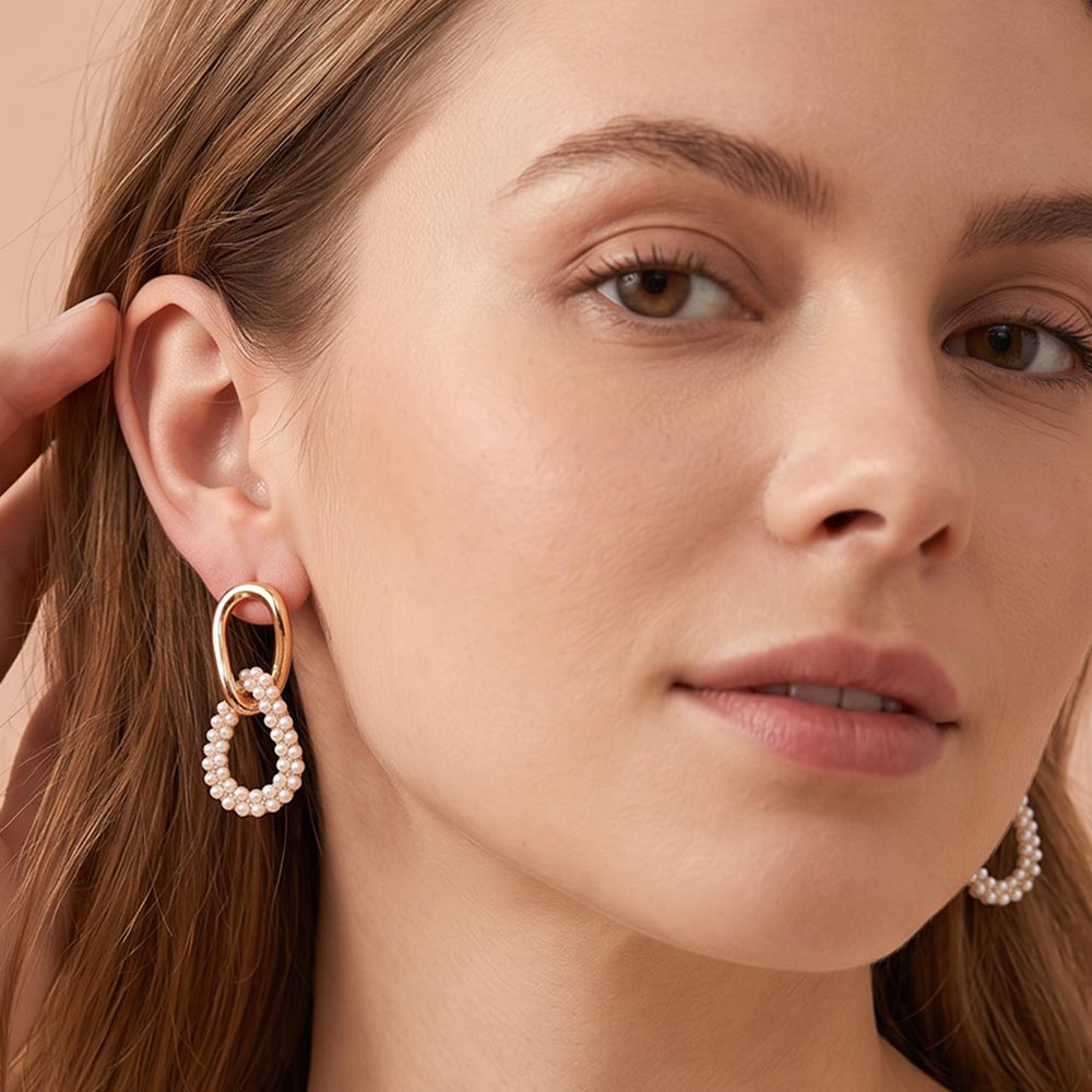 Model wearing gold-colored link drop earrings with small white bead accents