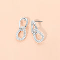 Silver-colored link drop earrings with small white bead accents on a peach background