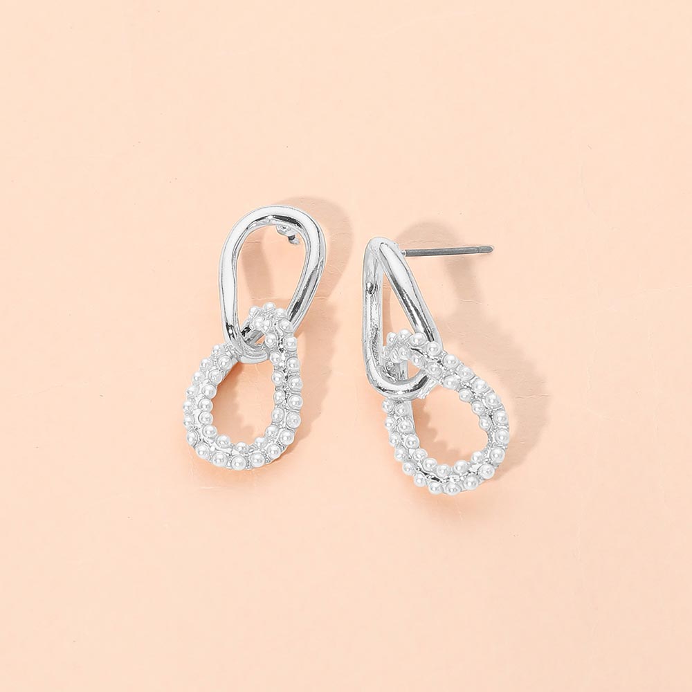 Silver-colored link drop earrings with small white bead accents on a peach background